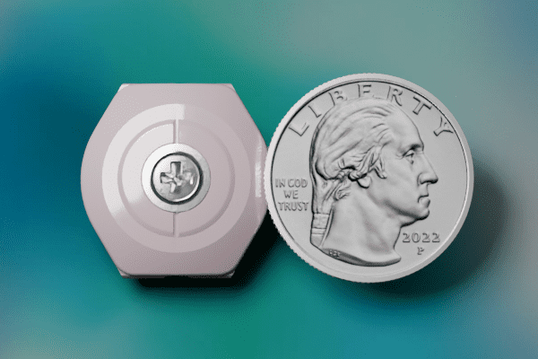 A small hexagonal device with a flower symbol next to a 2022 US quarter for size.